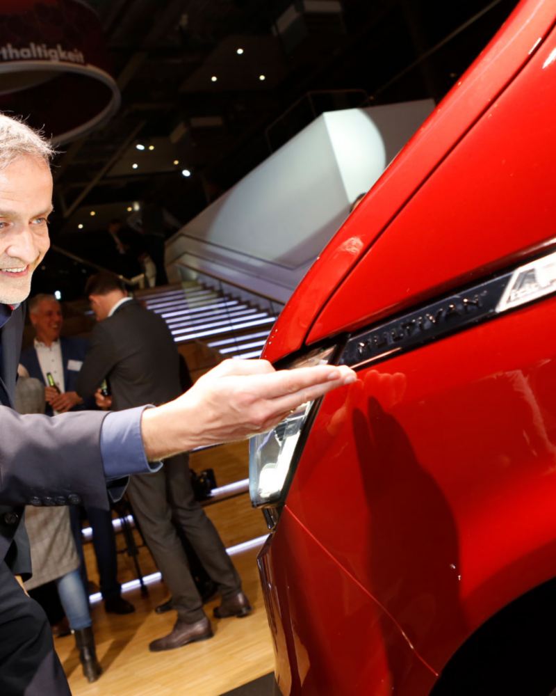Thomas Sedran pekar på framlampan på en röd VW Multivan T6.1