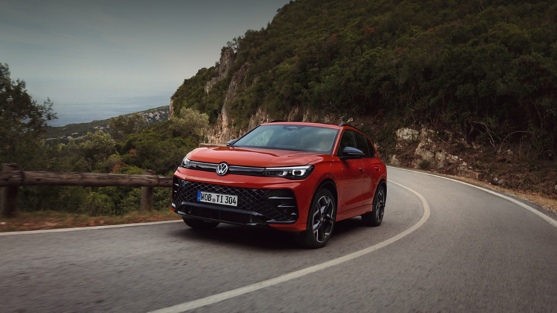 A red Volkswagen Tiguan SUV being driven on a curved rural road.
