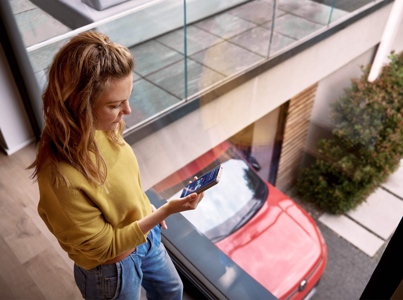 A woman looking at her smartphone above a red VW Tiguan