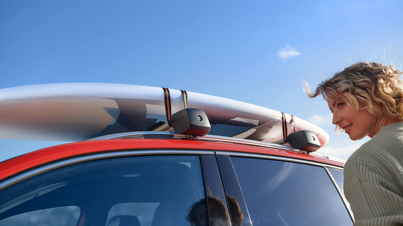 A surfboard sitting on a roofrack of a red VW Tiguan