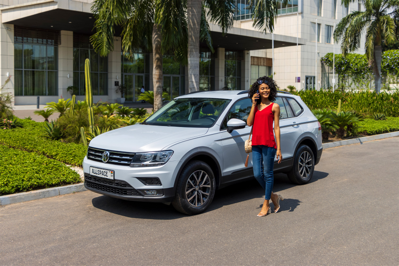woman in red top standing next to white  Volkswagen Tiguan Allspace