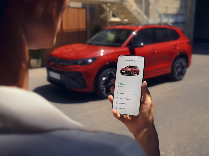 A woman holding a smartphone, with a red VW Tiguan in the distance