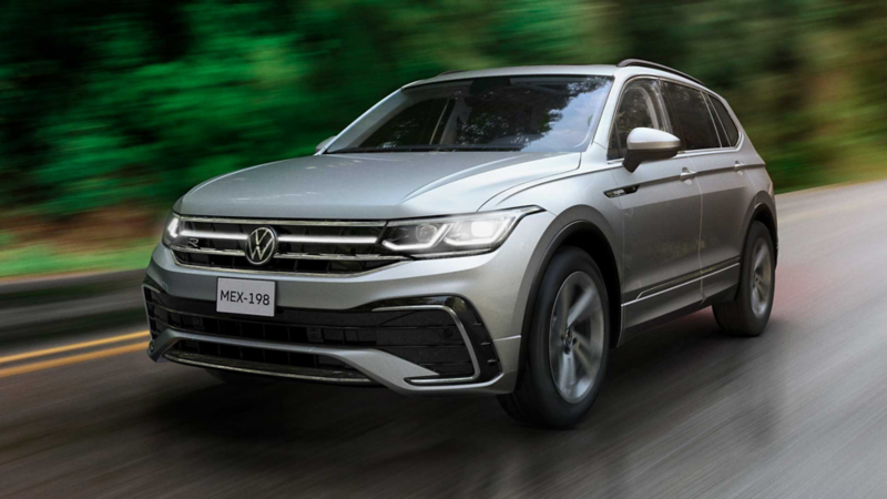 Volkswagen Tiguan en color plata dentro de carretera boscosa. 