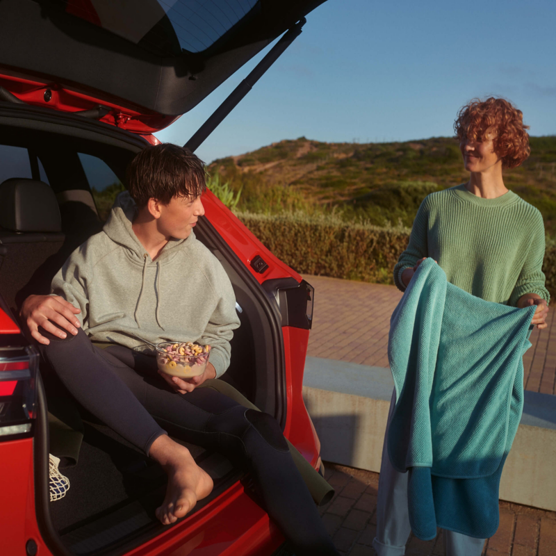 A young man sitting in the boot of a VW Tiguan with a woman standing next to him