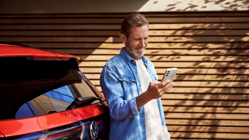 A man standing behind a red VW Tiguan and looking at his smartphone