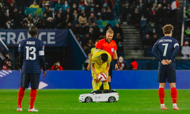 Les joueurs de l'Equipe de France de football entoure la Tiny ID.4 en action sur le terrain.