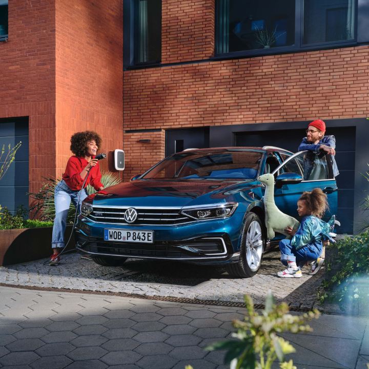 Un padre y una madre junto a su hija en un Volkswagen de color azul oscuro estacionado en la calle