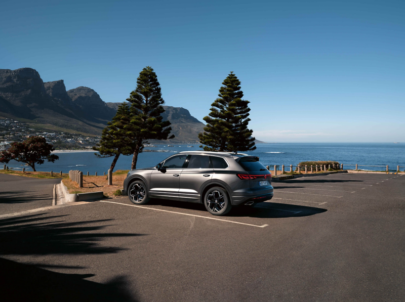 A VW Touareg parked next to a tree with the sea in the background