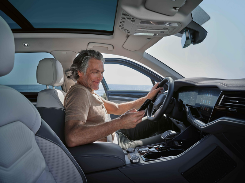 A man looking at a smartphone sitting in the driver's seat of a VW Touareg