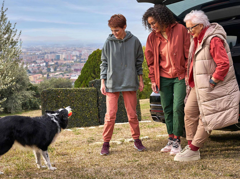 Three women stand beside a VW Touareg while looking at a nearby dog
