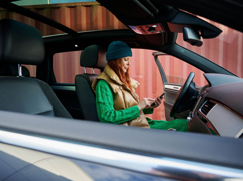 A woman looking at a smartphone while sitting in the driver's seat of a VW Touareg