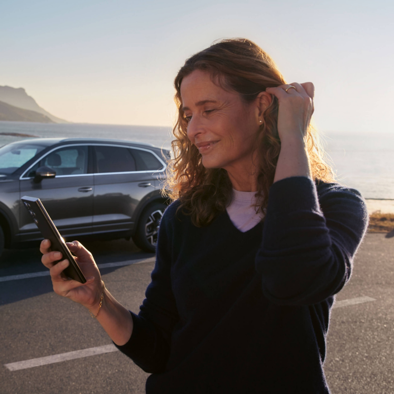 A woman looking at a smartphone standing next to a VW Touareg