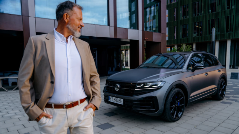 Doradca samochodowy i klientka stoją przed autem widocznym z boku.