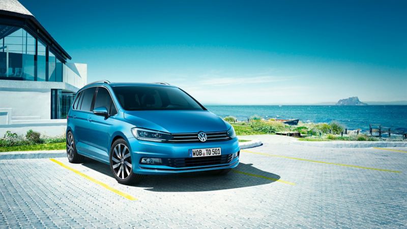 VW Touran bleu garé devant une maison vers la plage