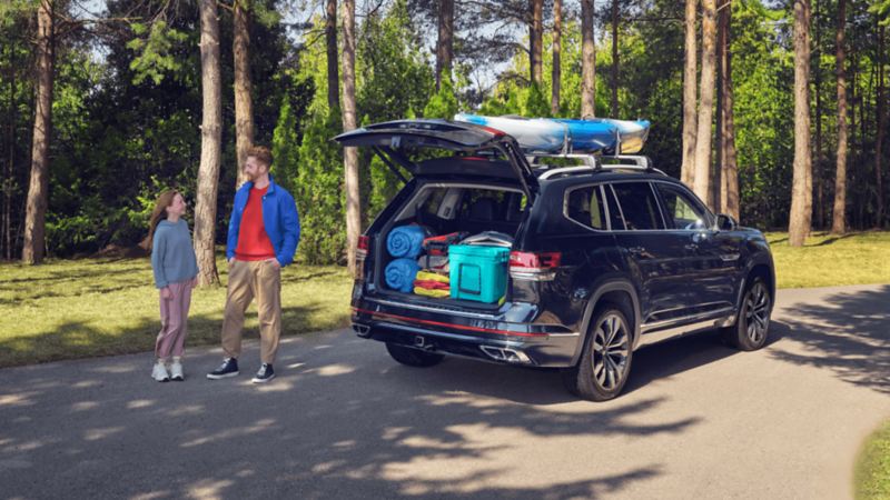 Un père et sa fille se tiennent à côté d’un VWUS Atlas 2022 de Volkswagen bleu tourmaline métallisé avec le coffre ouvert sur l'espace de chargement.