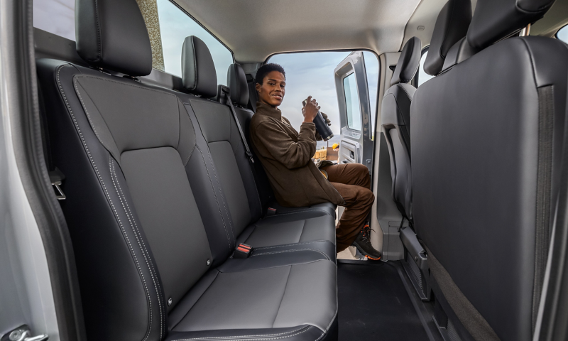 Rückbank eines VW Transporters, auf dem linken Sitz sitzt eine Person mit Thermoskanne in der Hand.