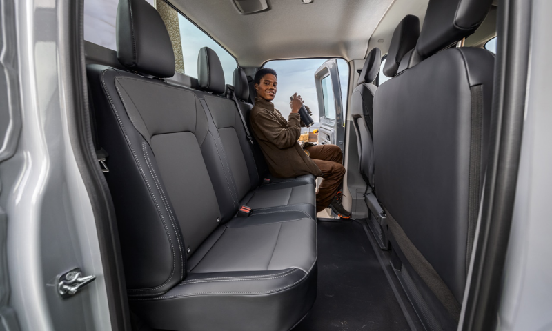 Eine Bauarbeiterin sitzt auf der zweiten Sitzreihe im VW Transporter und macht Pause.