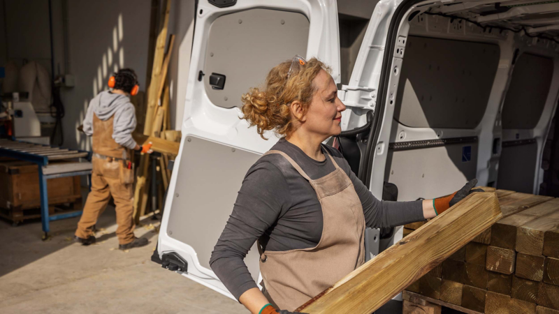 A construction worker loading wooden planks into the load compartment of a New Transporter. 