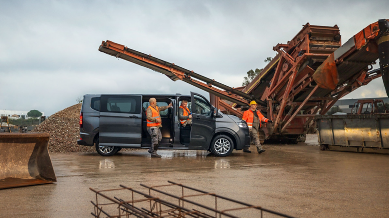 Des ouvriers sortent d’un VW Transporter Combi, avec en arrière-plan un chantier de construction avec des machines.
