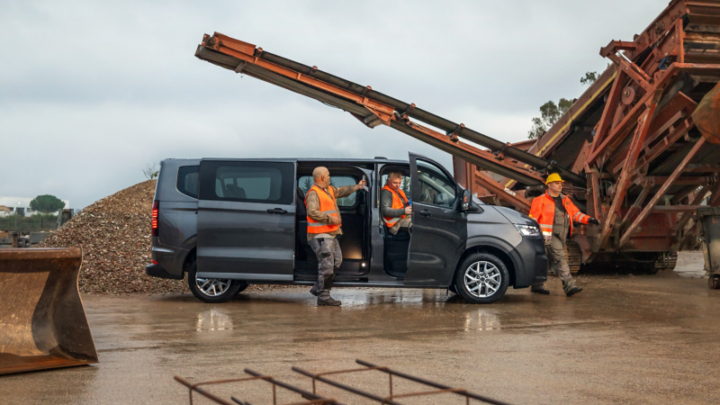 VW Transporter Kombi parkt auf einer Baustelle. Bauarbeiter steigen aus dem Fahrzeug.