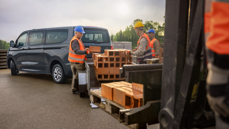 Bauarbeiter entladen Material aus einem VW Transporter Kombi.
