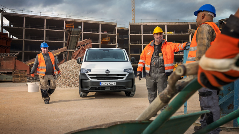 Une vue de devant du nouveau VW Transporter blanc sur un chantier avec des ouvriers