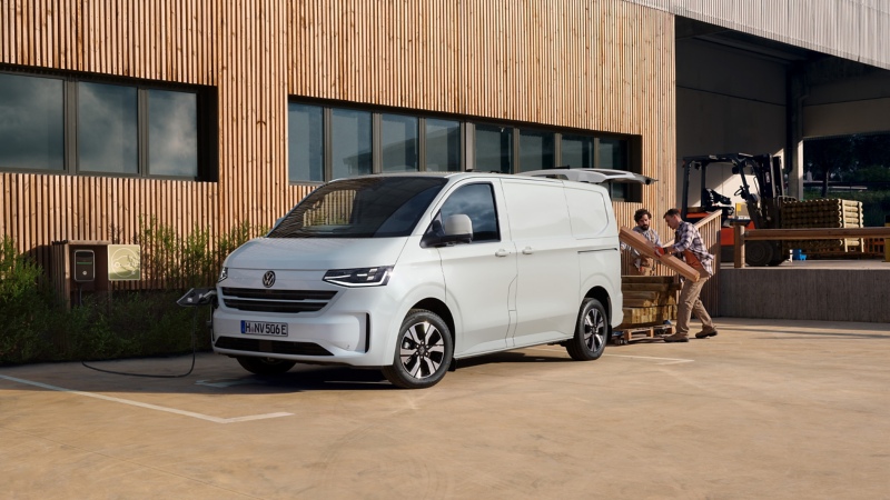 VW e-Transporter Kastenwagen steht an einer Ladesäule und wird mit Holzbalken beladen.