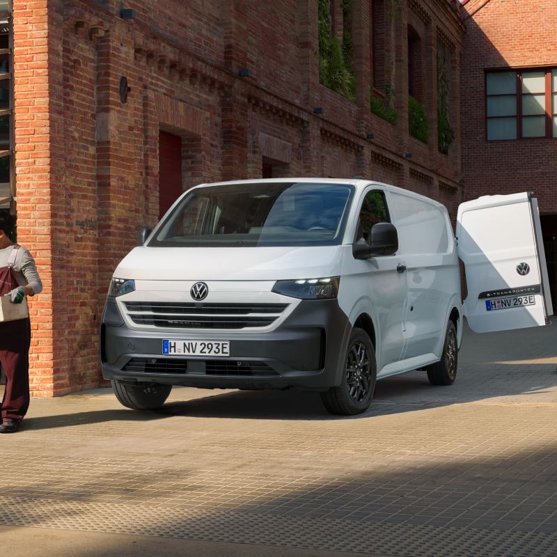 VW e-Transporter parkt neben einem Café. Lieferanten entladen Obst- und Gemüsekisten aus dem Heck des Fahrzeugs.