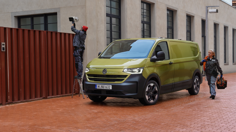 Zwei Monteure bringen eine Kamera an einer Hauswand an. Daneben steht der VW Transporter Kastenwagen.