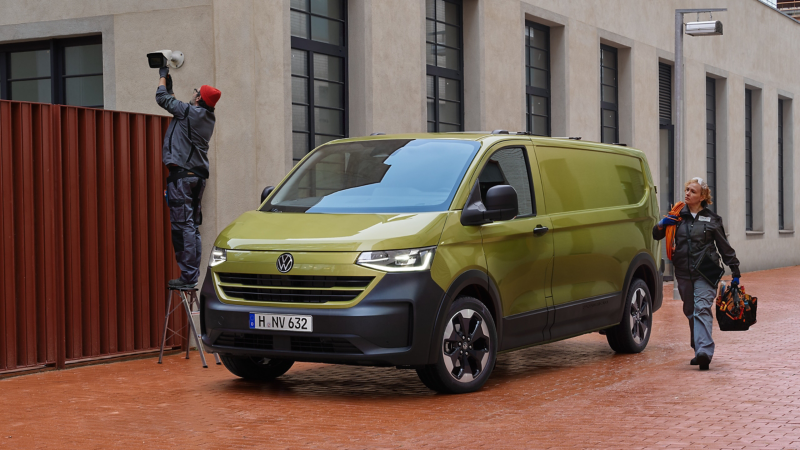 Zwei Monteure bringen eine Kamera an einer Hauswand an. Daneben steht der VW Transporter Kastenwagen.