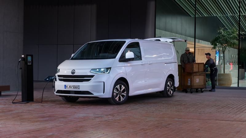 VW Transporter Kastenwagen eHybrid parkt an einer Ladesäule und wird mit Kisten beladen.