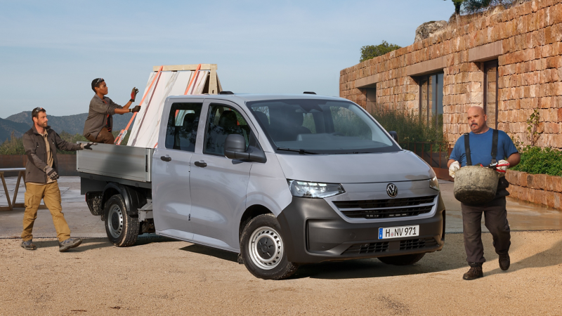 Handwerker laden etwas aus einem VW Transporter Pritschenwagen.