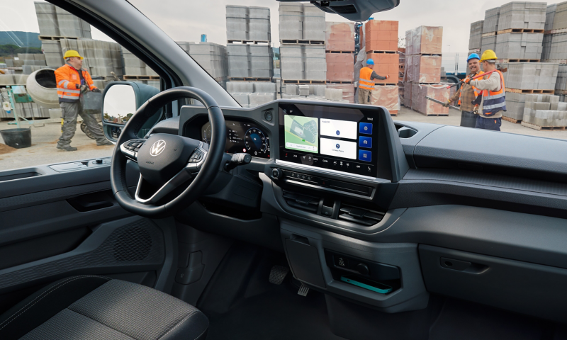 Das Cockpit eines VW Transporters, draußen stehen Bauarbeitern vor Baumaterialien.