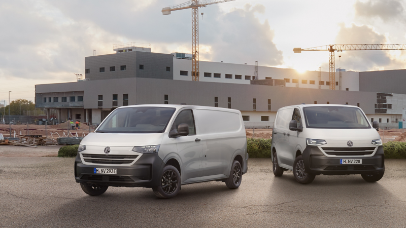 Ein VW Transporter und ein VW e-Transporter parken vor einer großen Baustelle