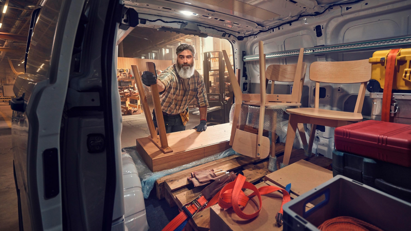 Ein Tischler verstaut Holzmöbel in einem VW Transporter.
