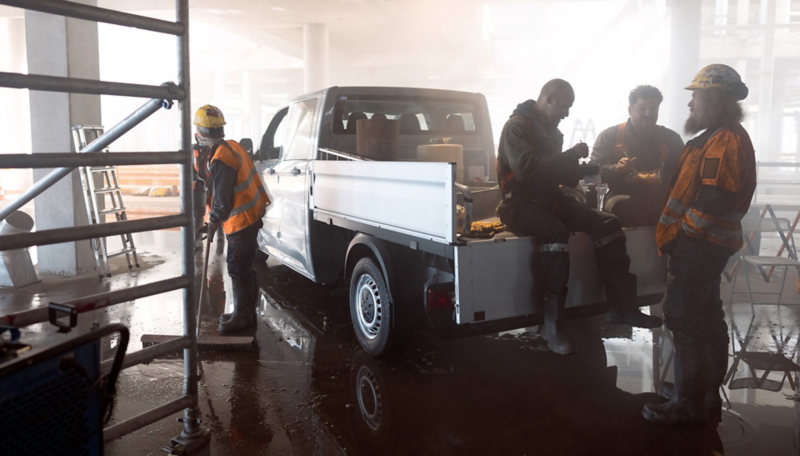 Mehrere Bauarbeiter pausieren um einen VW Crafter Pritschenwagen.