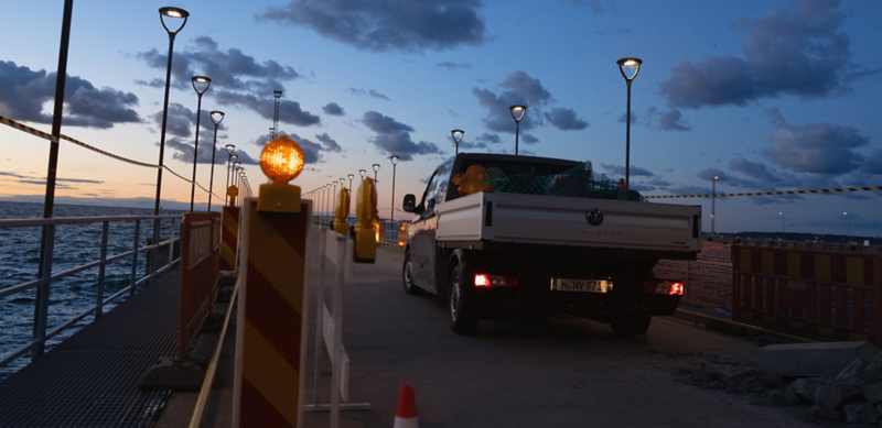 Ein VW Crafter Pritschenwagen parkt auf einer Baustelle am Wasser.