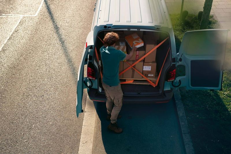 Un coursier charge sa camionnette VW Transporter de colis.