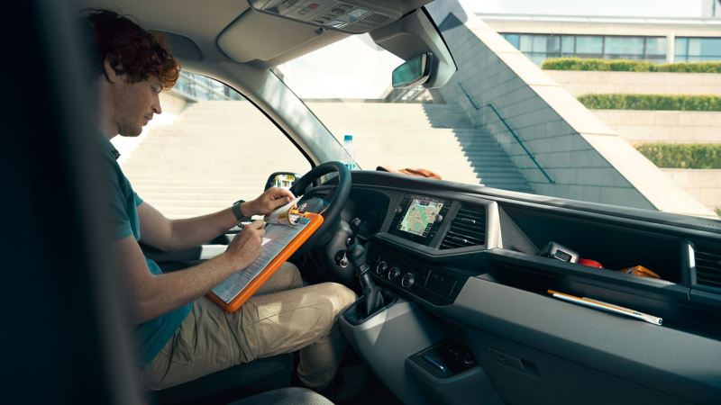 Ein Mann füllt auf dem Fahrersitz eines VW Transporter 6.1 einen Zettel auf einem Klemmbrett aus.