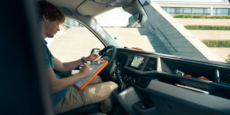 Ein Mann auf dem Fahrersitz eines VW Transporters schreibt auf ein Klemmbrett.