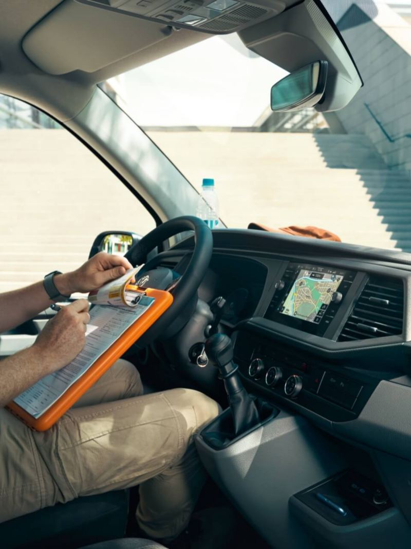 Ein Mann auf dem Fahrersitz eines VW Transporters schreibt auf ein Klemmbrett.