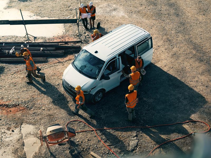 Ein VW Transporter auf einer Baustelle. Einige Bauarbeiter um das Fahrzeug rum.
