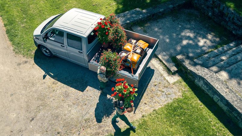 Zwei Gärtner entladen einen Volkswagen Nutzfahrzeuge Pritschenwagen.