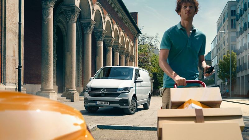 In the foreground a man is pushing a parcel van, in the background is a VW Transporter 6.1.