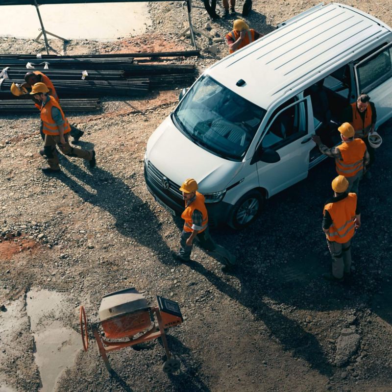 Ein VW Transporter 6.1 parkt auf einer Baustelle umgeben von Bauarbeitern.