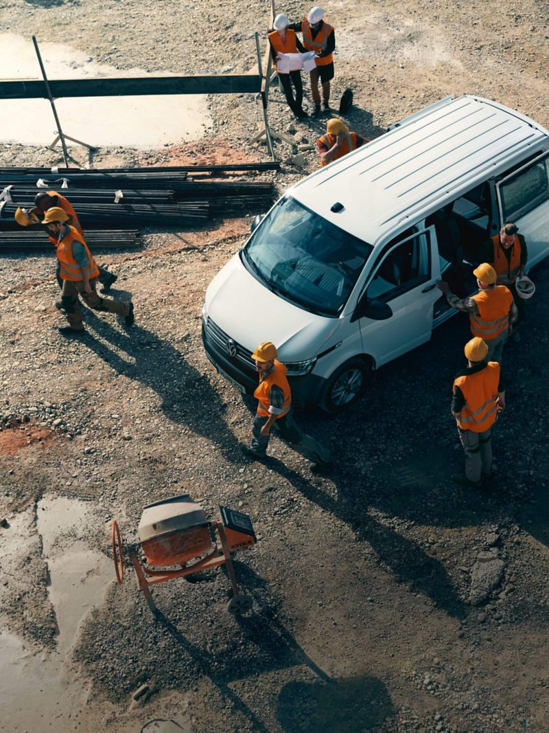 Ein VW Transporter 6.1 parkt auf einer Baustelle umgeben von Bauarbeitern.