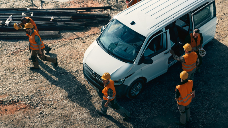 Einige Bauarbeiter stehen auf einer Baustelle um ihren Volkswagen Transporter 6.1 Kombi.