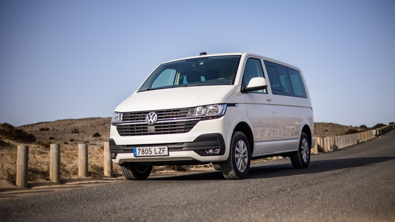 Una furgoneta Volkswagen Transporter blanca estacionada en una carretera sinuosa, con dunas de arena y vegetación seca a los lados, bajo un cielo despejado. La imagen transmite la robustez del vehículo en un paisaje natural.