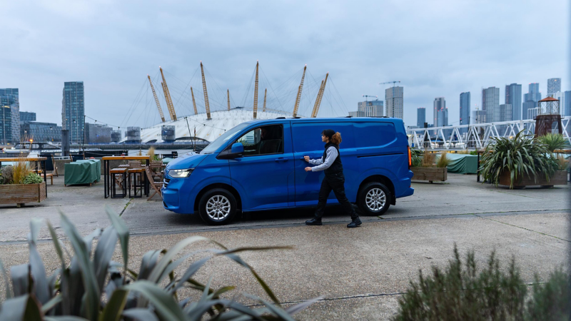 A woman standing in front of a VW Transporter parked in a docklands setting. 