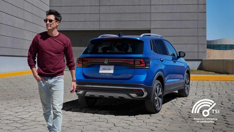 Joven conductor posa sobre SUV Taigun de Volkswagen, en color exterior azul. 